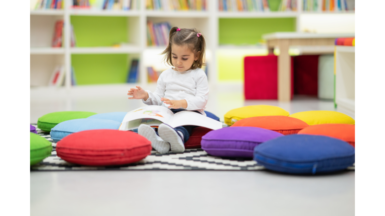 Cute girl is reading book sitting in nursery library