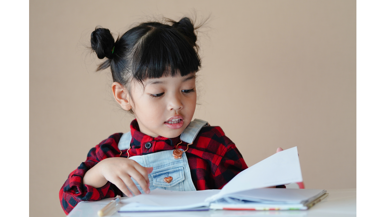 A cute preschool child Asian girl reading a book. Kids enjoy learning with happiness at home. Clever, Education, and smart learning concept.