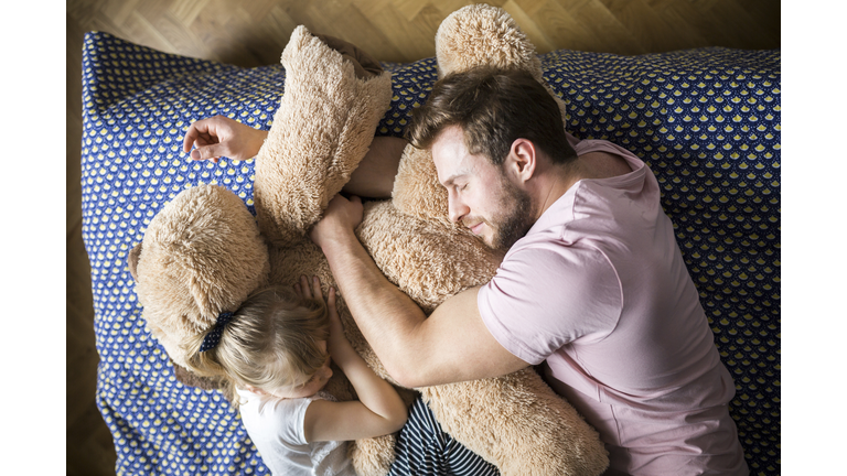 Father and daughter taking a nap, cuddling with teddy bear