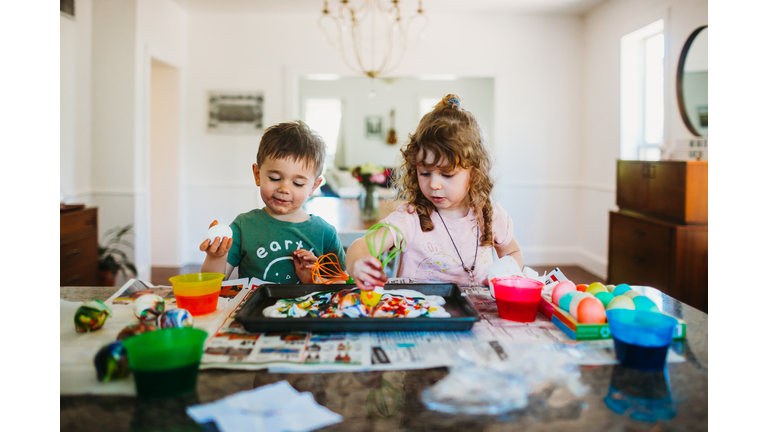 Young boy and girl sitting at kitchen counter dying easter eggs