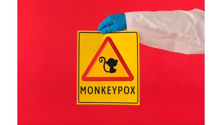 Arm of a doctor wearing a gown and latex gloves holding a yellow sign with a symbol with a monkey danger triangle and Monkeypox, on a red background. Pandemic, virus, epidemic, Nigeria and smallpox.