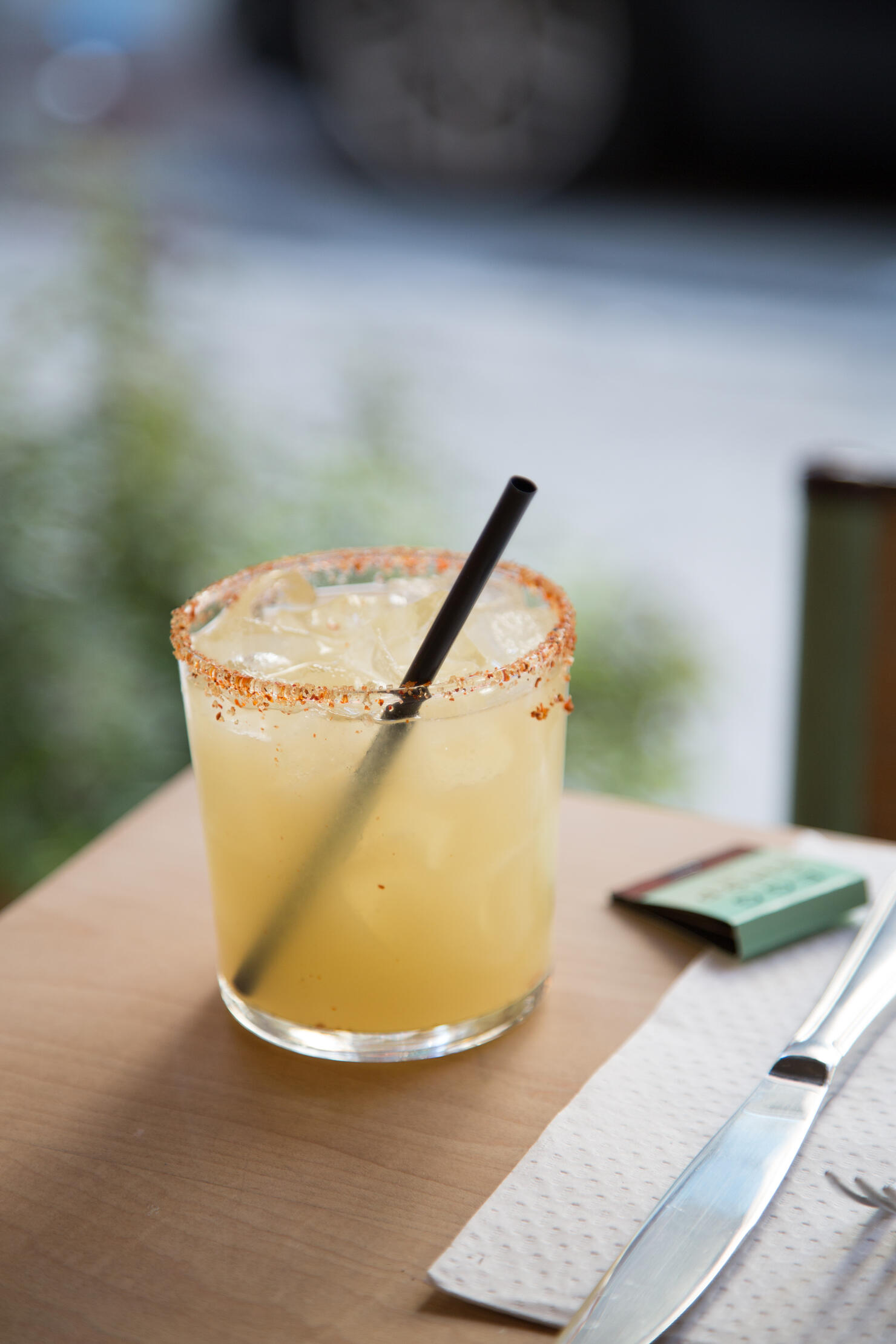 A Spicy Margarita sits on the edge of a table with street in background - Vertical