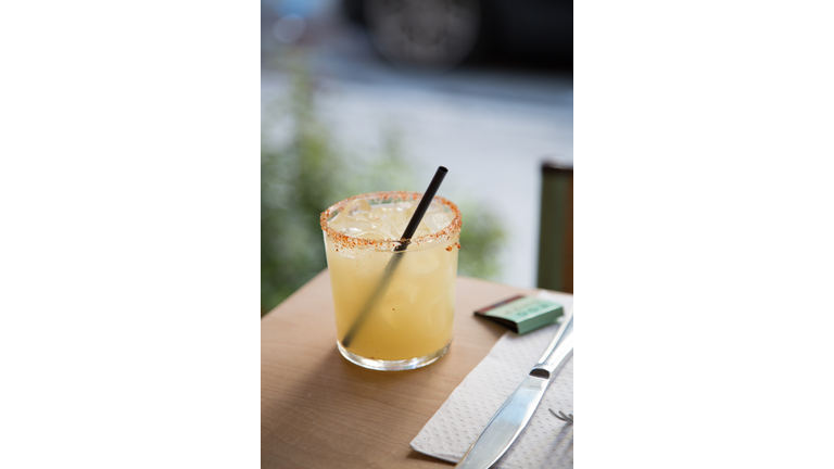 A Spicy Margarita sits on the edge of a table with street in background - Vertical