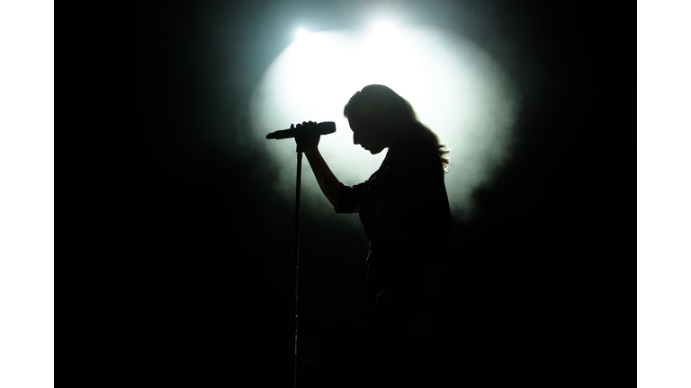 black silhouette of female singer with white spotlights in the background