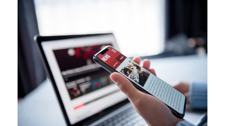 Online news on a smartphone and laptop, Woman reading news or articles in a mobile phone screen application at home. Newspaper and portal on internet.