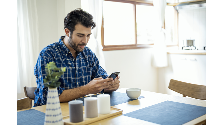 A Man using smartphone while sitting at dining table. Web Searching, Online dating, Text messaging.