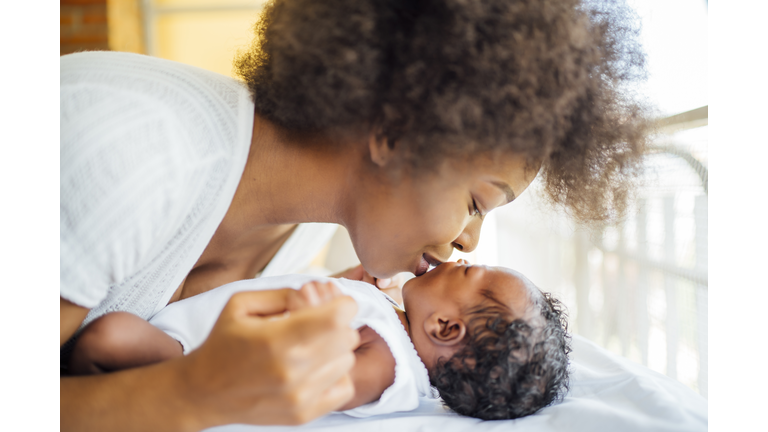 Close-up of mother kissing baby daughter lying on bed at home