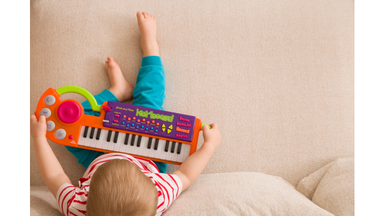 Top view on small cute toddler boy sitting on the sofa and playing on the toy piano. A little boy learning to play piano listening to music. Early development for toddler. Musical education for kids