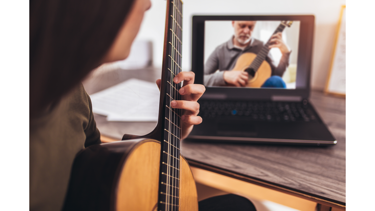 Happy little girl learning to play guitar while watching lessons at laptop at home