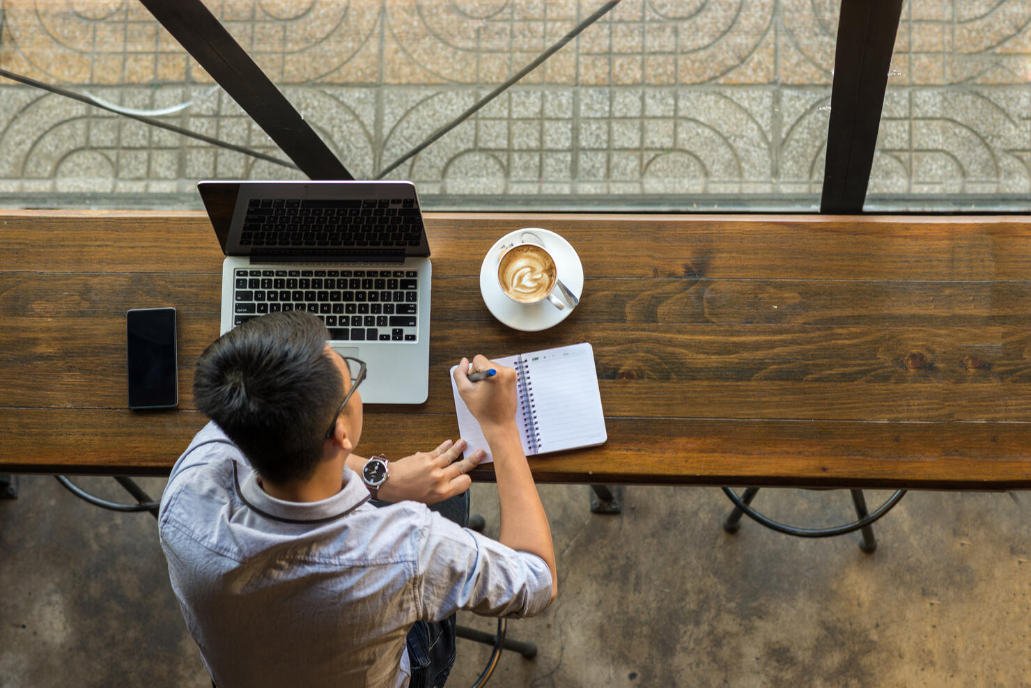 Young Asian businessman taking note beside laptop on wooden table