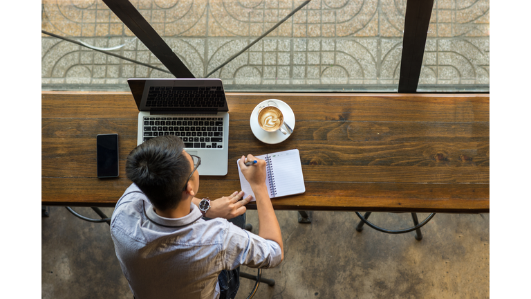 Young Asian businessman taking note beside laptop on wooden table