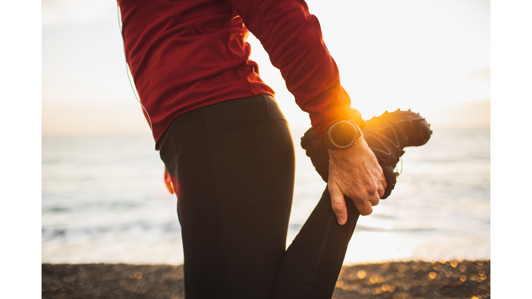 Male runner stretching leg and feet and preparing for running outdoors.