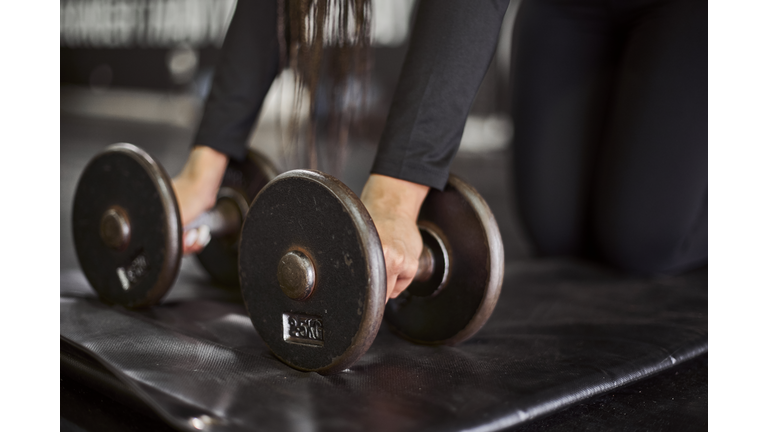 Close-up of young woman holding dumbbells on mat in gym