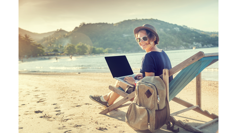 Young beautiful woman hipster traveler freelancer with laptop on the seashore. Business and vacation concept