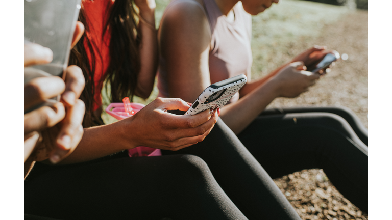 Three woman holding their mobile phones outside and looking at the screens