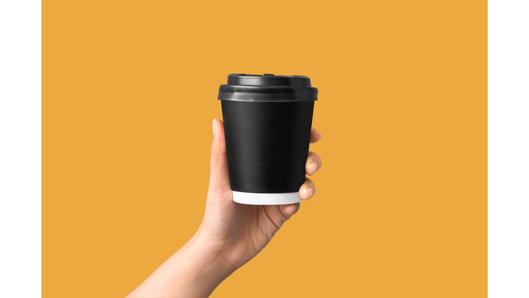 closeup of women hand holding paper coffee cup on yellow background