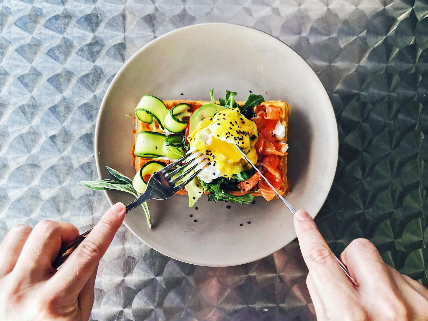 Eating brunch with waffle, avocado, cucumber, salmon and poached egg, personal perspective