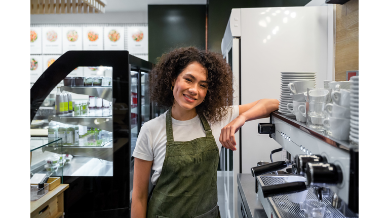 Content female barista standing near coffee machine in cafe