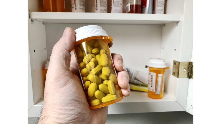 Man's hand holding bottle of prescription medication with medicine cabinet in background