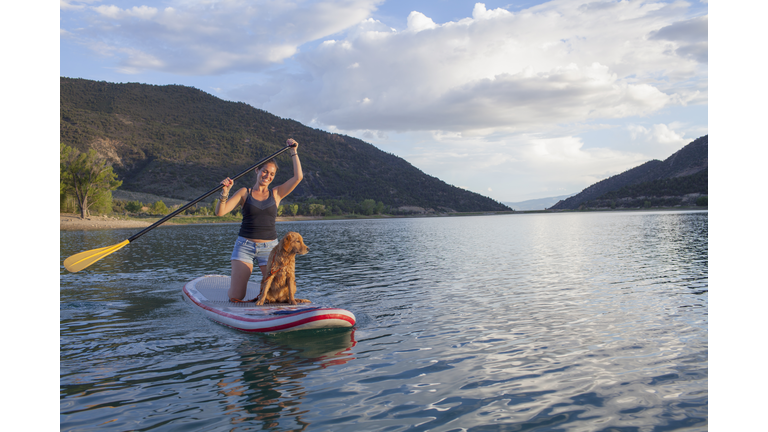Young woman paddleboarding with puppy on a lake