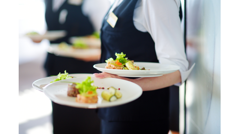 Waiter carrying plates with meat dish on some festive event