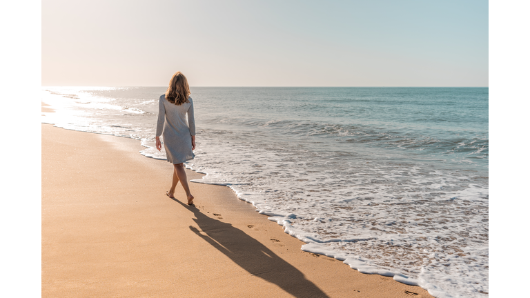 Woman walking on the beach looking at the sun