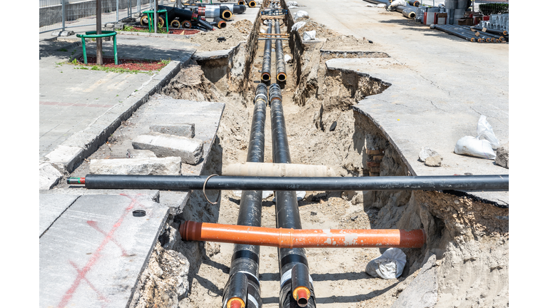 District heating pipeline reparation and reconstruction site parallel with the street with construction site safety net fence and insulated pipes for hot water in the trench before winter season come