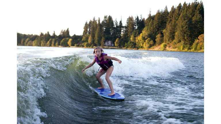 Young female wake surfing behind a ski boat