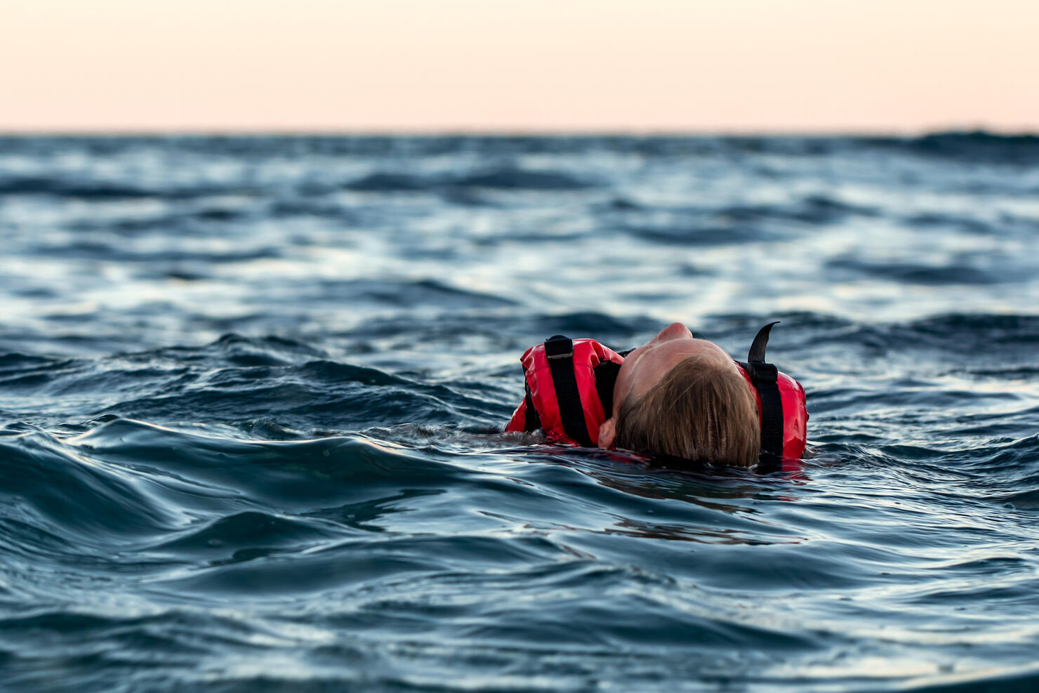Lifeless drowning girl in a life jacket on the high seas at dusk