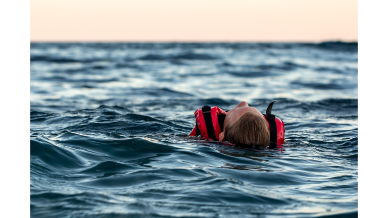 Lifeless drowning girl in a life jacket on the high seas at dusk