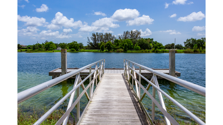 Ramp to boat dock or fishing platform on blue green lake with trees and blue sky - Vista View Park, Davie, Florida, USA