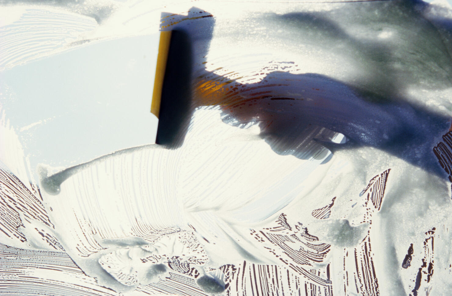 Person wiping soapy windscreen with squeegee, close-up