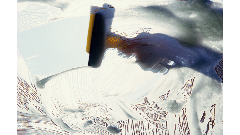 Person wiping soapy windscreen with squeegee, close-up