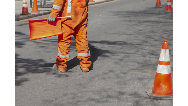 street construction zone with orange suited man directing traffic with orange flag