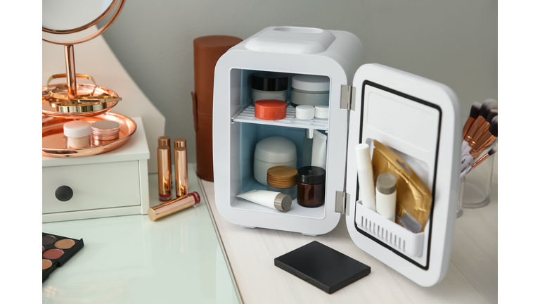 Cosmetics refrigerator and skin care products on white vanity table indoors