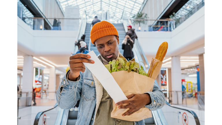 Surprised black man looks at receipt total with food in mall