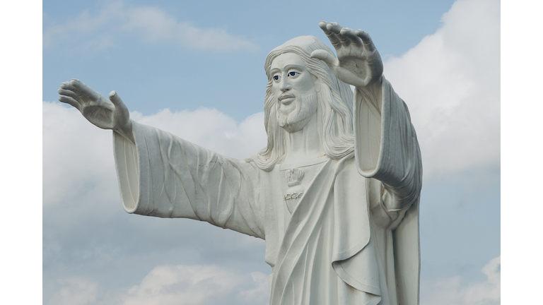 Jesus statue standing and blessing with both the hands against blue sky background.