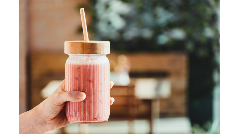 Young woman's hand with a red fruit smoothie.