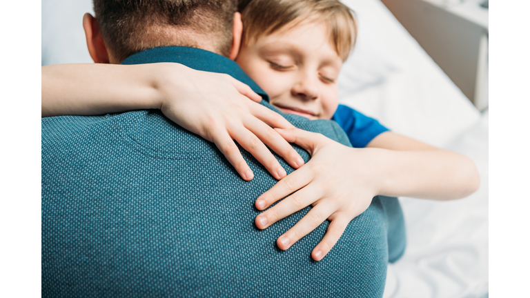 portrait of smiling little son hugging father in hospital chamber