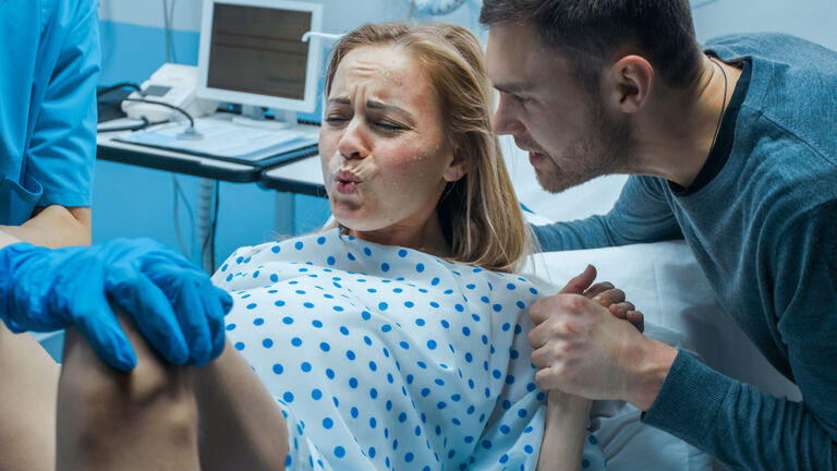 In the Hospital Close-up on Woman in Labor Pushes to Give Birth, Obstetricians Assisting, Husband Holds Her Hand. Modern Delivery Ward with Professional Midwives.