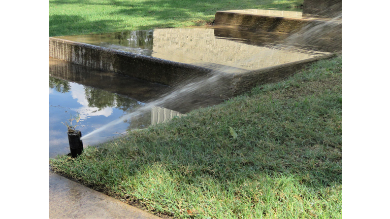 Water Sprinkler, Grass, Concrete. Wasting Water. Water Conservation.