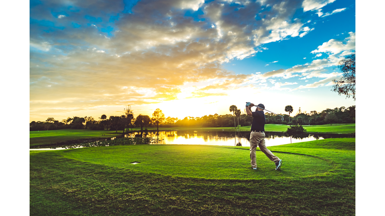 Man on a beautiful scenic sunset golf course swings a golf club