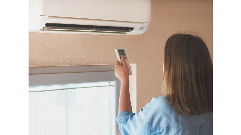 Woman holding remote control aimed at the air conditioner.