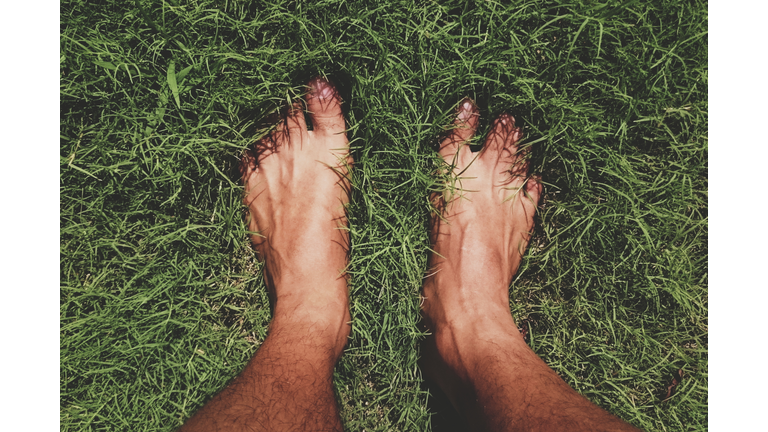 Low Section Of Man Standing On Grassy Field