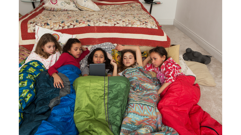 Girls in sleeping bags at slumber party using digital tablet