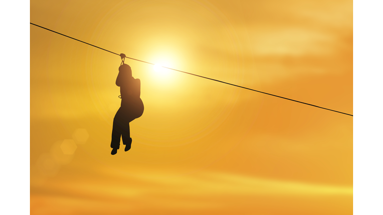 silhouette of side view of young woman riding on zip line on sunset background.
