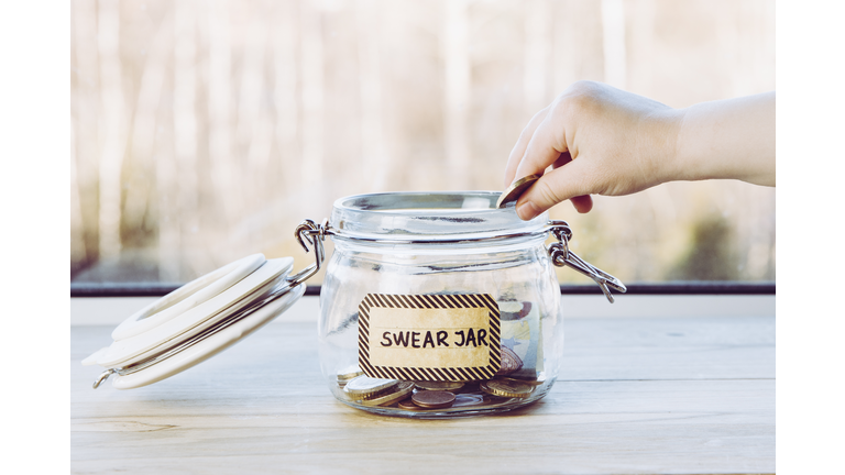 Selective focus on child hand, put euro coin in swear jar. Every time child curses or swears it has to put money as punishment in jar for safe keeps. Bad habit concept.
