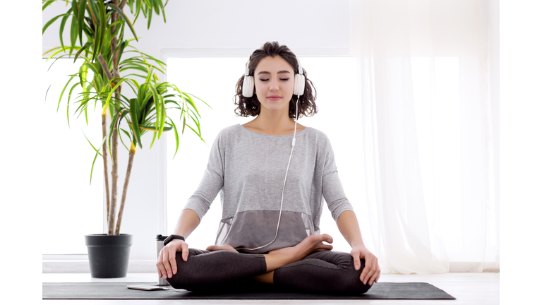 Modern woman with headphones sitting in yoga lotus posture