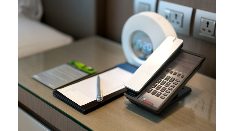 Black telephone and note in front and bed in the background, focus on the telephone,for room service,communication themes in hotel or resort.