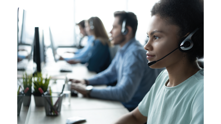 How can I help you? Beautiful call center workers in headphones are working at modern office